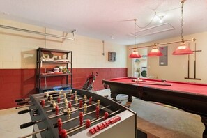 Une pièce avec un baby-foot, une table de billard et un mur rouge.