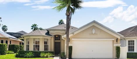 A residential house with a garage, a well-maintained lawn, and a palm tree.