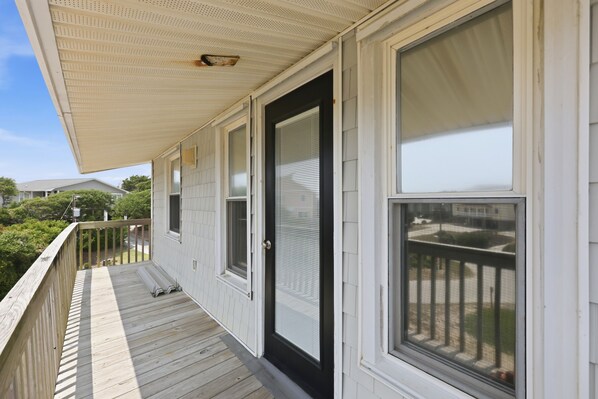 A covered porch with a black door and windows, wooden railing, and a view of the neighborhood. - Dolphin Reach Lower | Steps to Beach + Deck (Emerald Isle)