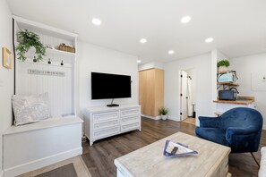 A modern living room with a flat-screen TV, a blue armchair, and a wooden coffee table. - Dolphin Reach Lower | Steps to Beach + Deck (Emerald Isle)