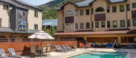 Un hotel con piscina, sillas de descanso y vistas a una montaña boscosa.
