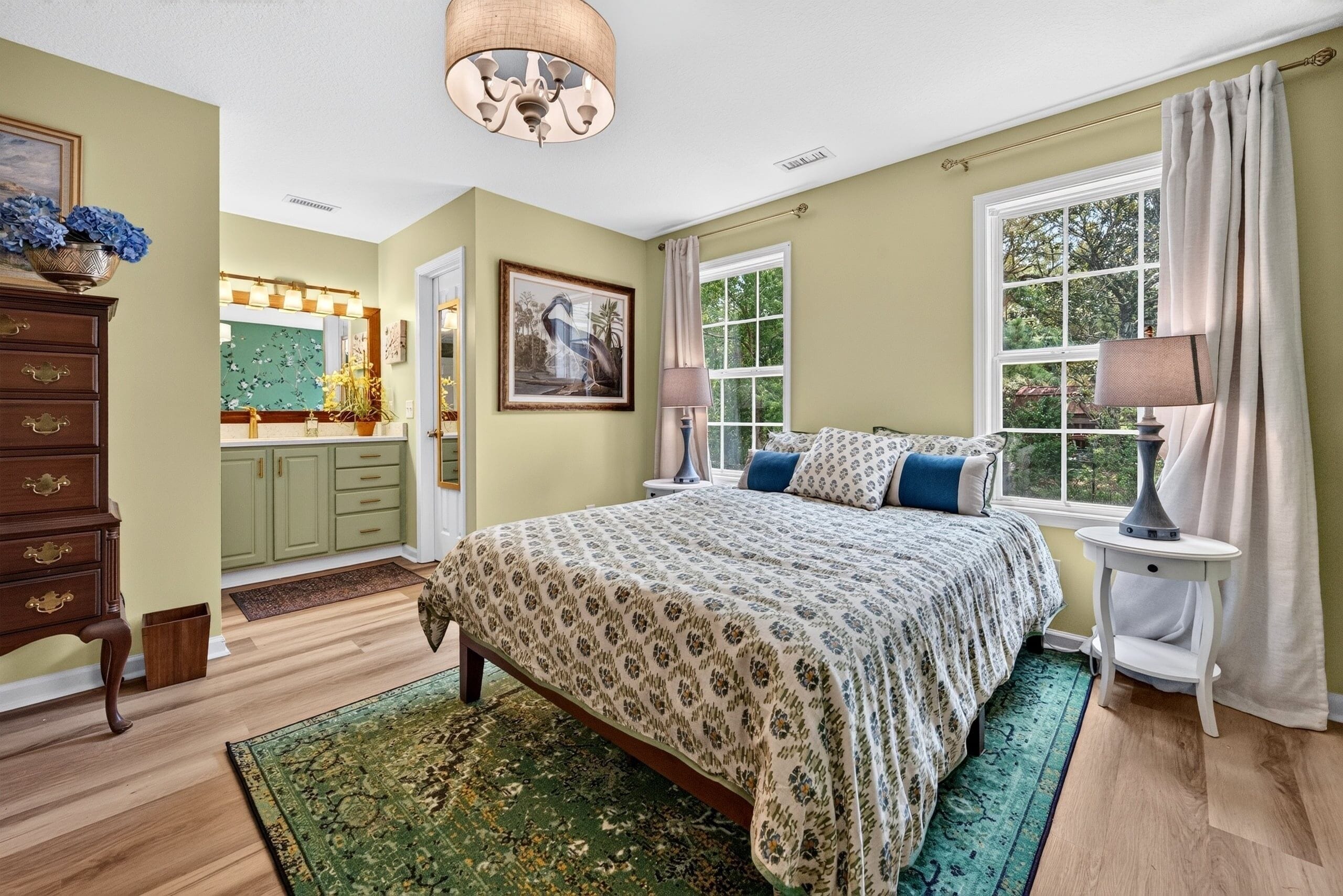 A bedroom with a large bed, a dresser, a window with curtains, and a chandelier.