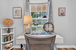 A room with a desk, chair, bookshelves, a lamp, a clock, and framed artwork. - Sweetgrass Cottage 3 Bedroom Home (Georgetown)