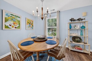 Un comedor con mesa de madera, sillas, una araña y obras de arte en las paredes.