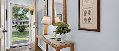 Un pasillo con una consola de madera, una lámpara, un espejo e impresiones botánicas enmarcadas en la pared.