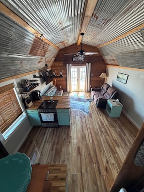 A cozy cabin interior with a kitchen, dining area, and a living room with a couch and a ceiling fan.