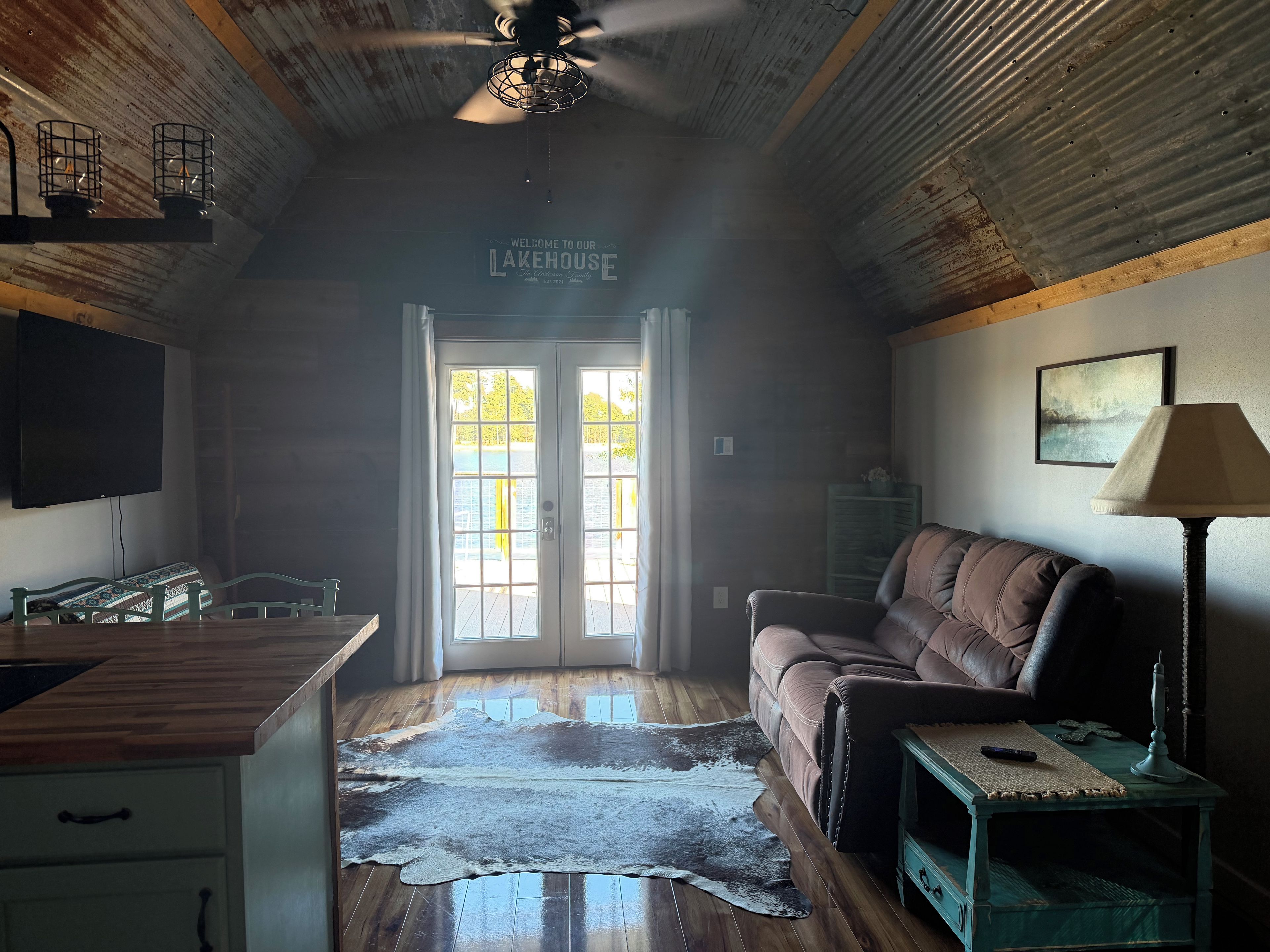 A room with a wooden ceiling, a ceiling fan, a television, a couch, a lamp, and a rug.