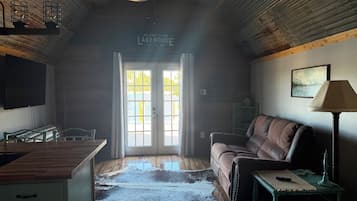 A room with a wooden ceiling, a ceiling fan, a television, a couch, a lamp, and a rug.