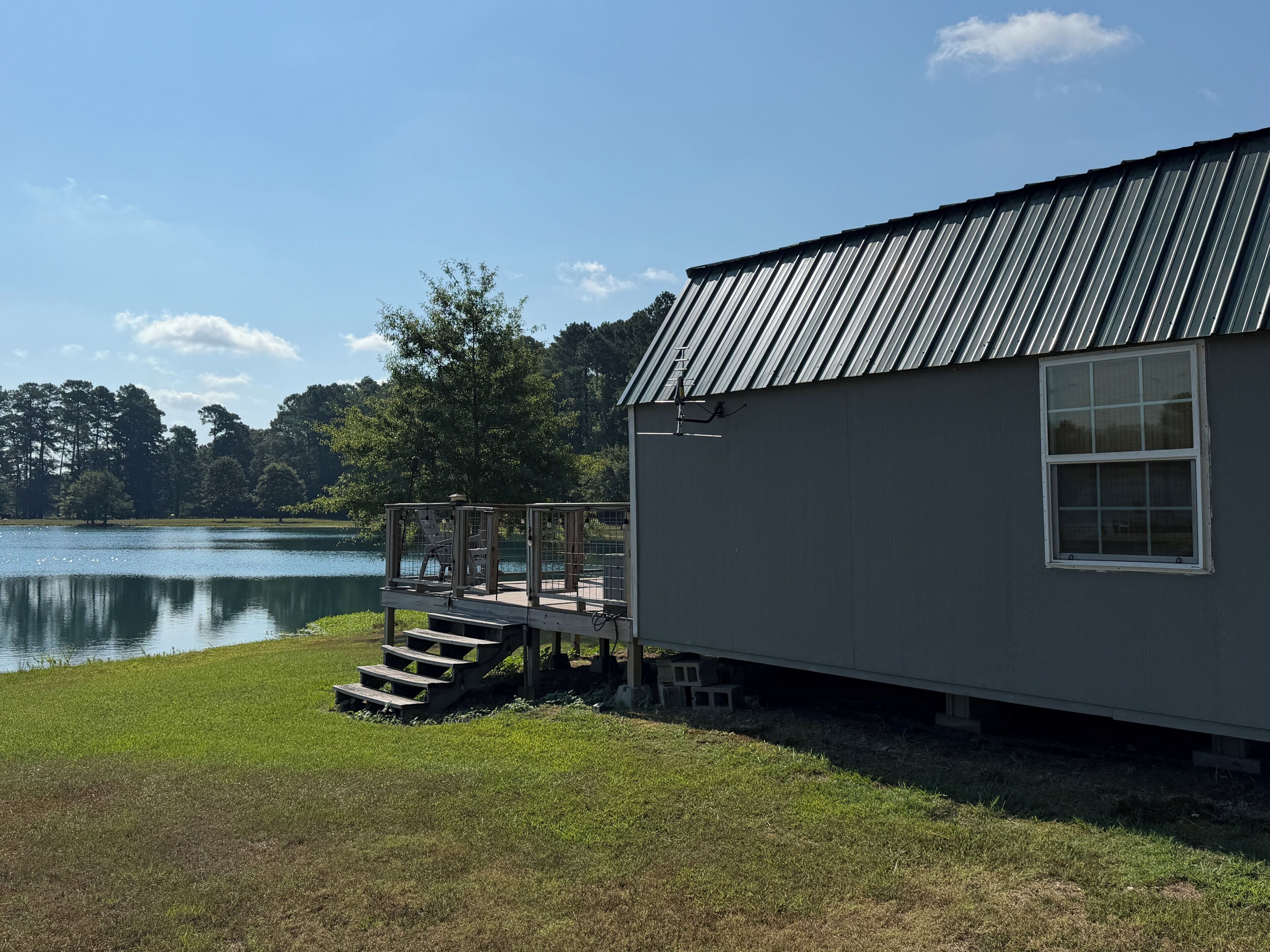 A small cabin with a metal roof, a wooden deck, and a view of a lake.