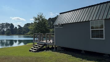 A small cabin with a metal roof, a wooden deck, and a view of a lake.