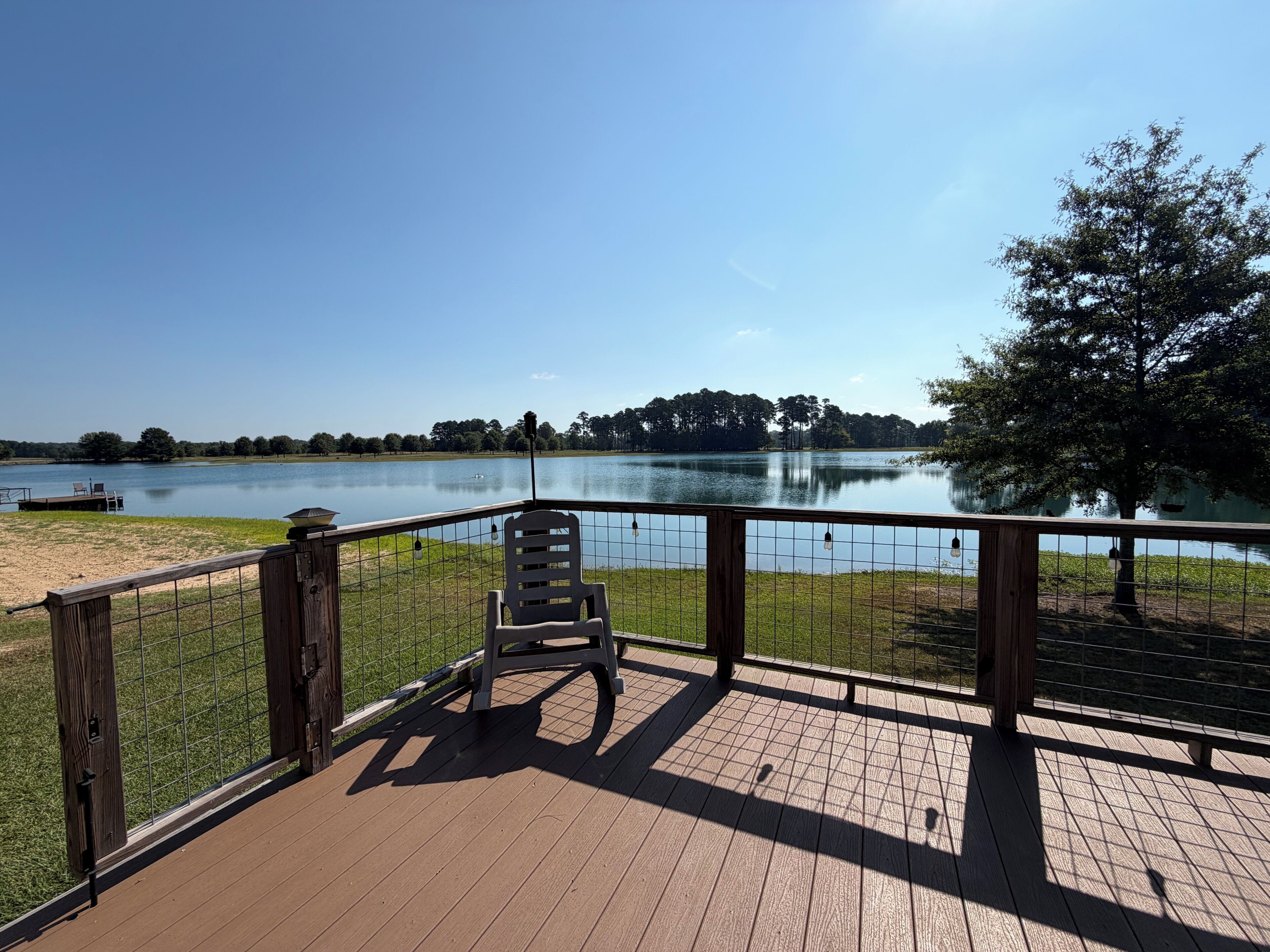 A wooden deck with a chair, overlooking a calm lake with a clear sky.
