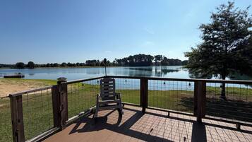 A wooden deck with a chair, overlooking a calm lake with a clear sky.