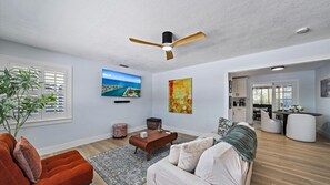 A modern living room with a flat-screen TV, a ceiling fan, and a dining area with a table and chairs. - Hemingway Hideaway 2 Bedroom Home (Sarasota)