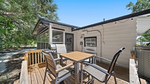 A deck with a grill and chairs, a wooden table, and a view of a garden. - Hemingway Hideaway 2 Bedroom Home (Sarasota)