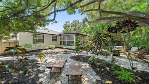 A house with a covered patio, outdoor seating, and a garden with various plants. - Hemingway Hideaway 2 Bedroom Home (Sarasota)
