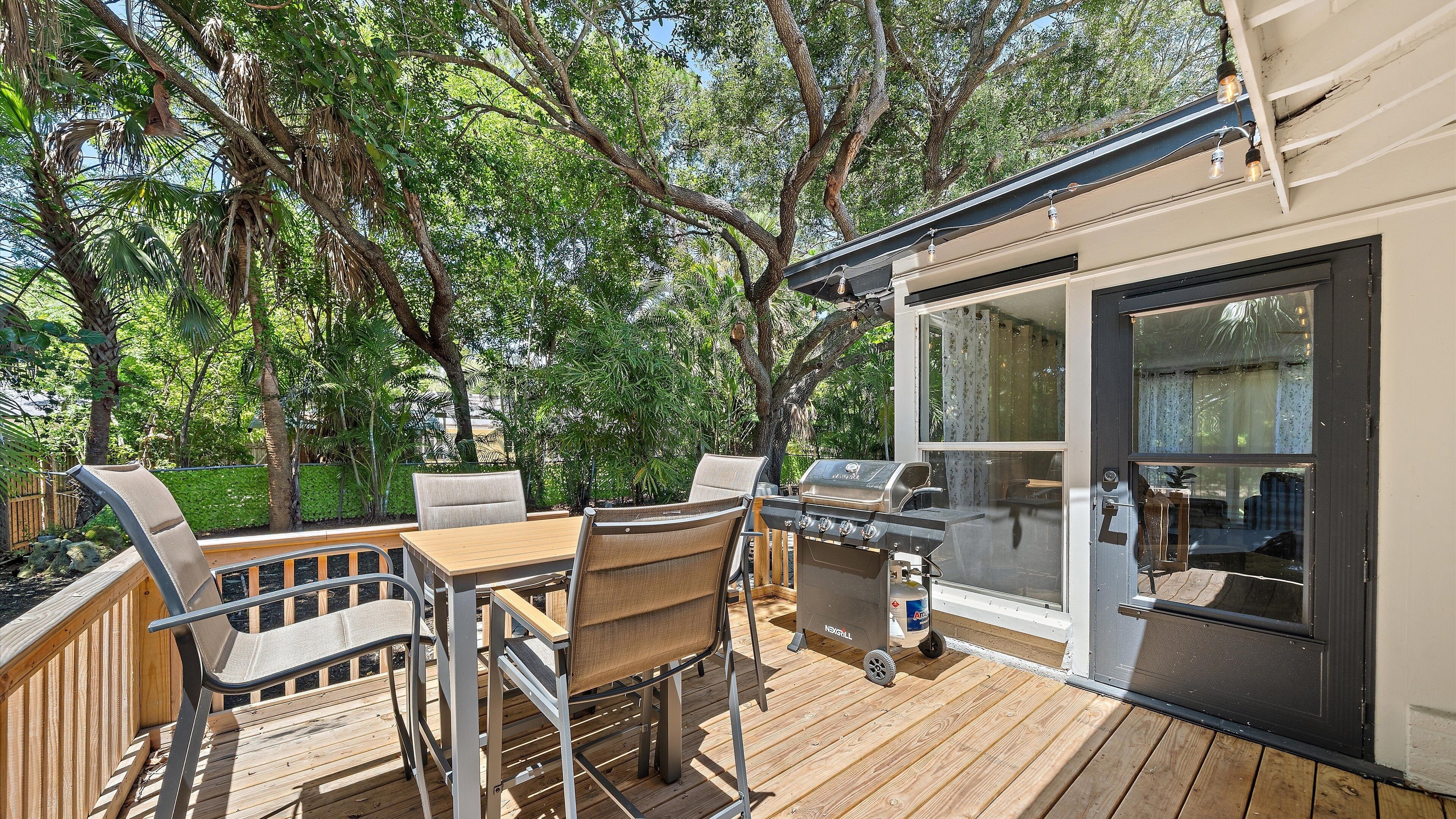 An outdoor deck with a grill, chairs, and a table.