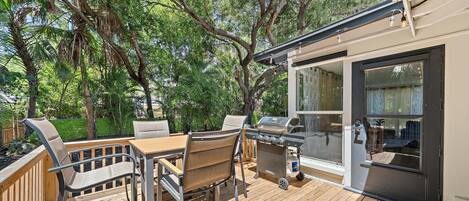 An outdoor deck with a grill, chairs, and a table.