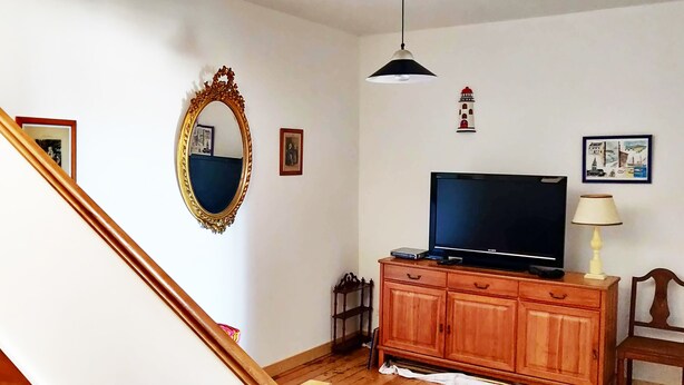 A staircase leading to a living area with a television, wooden cabinet, and decorative items on the wall. - Quiet house in the city center (Douarnenez)