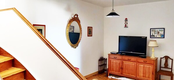 Eine Treppe führt zu einem Wohnbereich mit Fernseher, Holzschrank und dekorativen Gegenständen an der Wand.