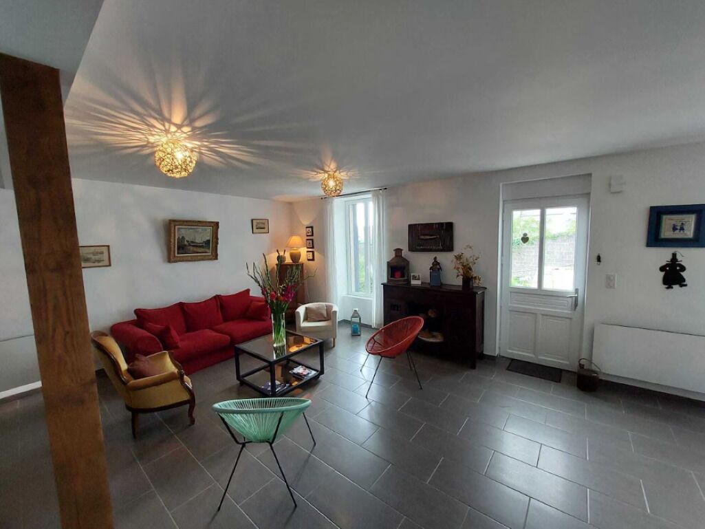Un salon avec un canapé rouge, une table basse et un fauteuil. On y trouve deux lampes suspendues et une porte avec une fenêtre.