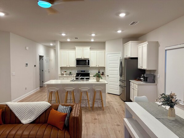 A modern kitchen with white cabinets, a central island with bar stools, a refrigerator, and a microwave. - SunFish - 4-bedroom home in gorgeous Port St. Joe with private in-law suite (Port St. Joe)