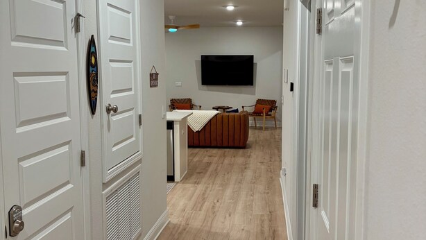 Un pasillo con puertas blancas, un televisor de pantalla plana en la pared y una zona de estar con una mesa y sillas.