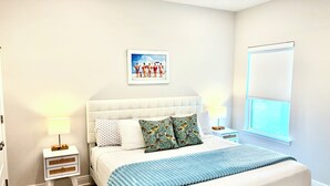 Un dormitorio con una cama grande, una mesita de noche con lámpara, un cuadro en la pared y una ventana.