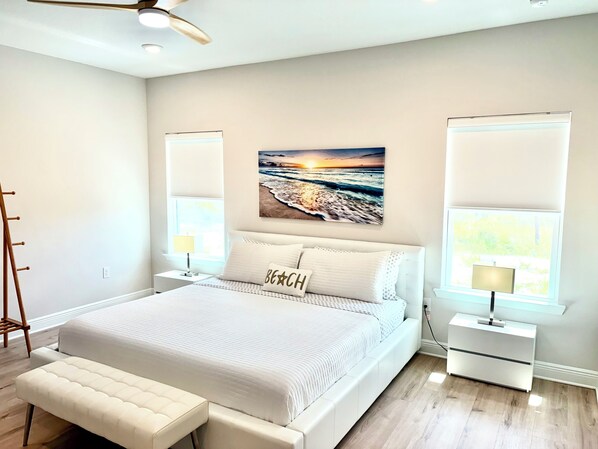 Een slaapkamer met een groot bed, nachtkastjes, een bankje en een plafondventilator.