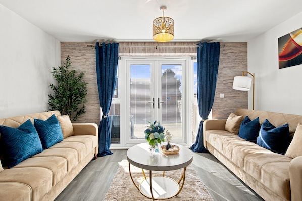A modern living room with two sofas, a coffee table, and a large window with blinds. - Stylish 2BR House/Garden/Free Parking/Alton Towers (Stoke-on-Trent)