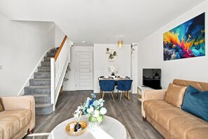 Ein modernes Wohnzimmer mit Treppe, Essbereich und einem großen abstrakten Gemälde.