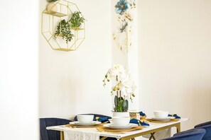 Ein Esstisch ist mit weißen Tellern, goldbesteck und einer Vase mit weißen Blumen gedeckt.