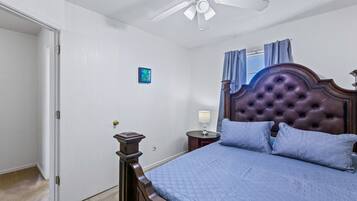 Un dormitorio con cama, ventilador de techo, mesita de noche y ventana con cortinas.