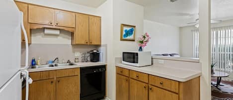 Una cocina compacta con armarios de madera, horno empotrado, microondas y un lavabo.