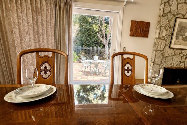 A dining table with two chairs, a glass of wine on each chair, and a view of a garden through a glass door. - 80`s Oldies Speakeasy Estate - 5 BD - AC (San Diego)