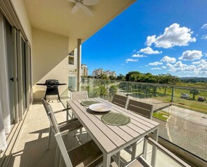 Ein Balkon mit Tisch, Stühlen, einem Grill und Blick auf Gebäude und Grünflächen.