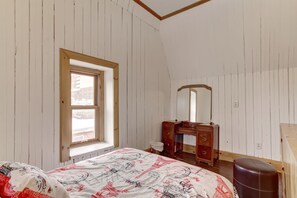 A bedroom with a single bed, a wooden dresser, a mirror, and a window.