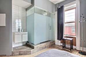A modern bedroom with a glass shower enclosure, a wooden floor, and a view of the outside.