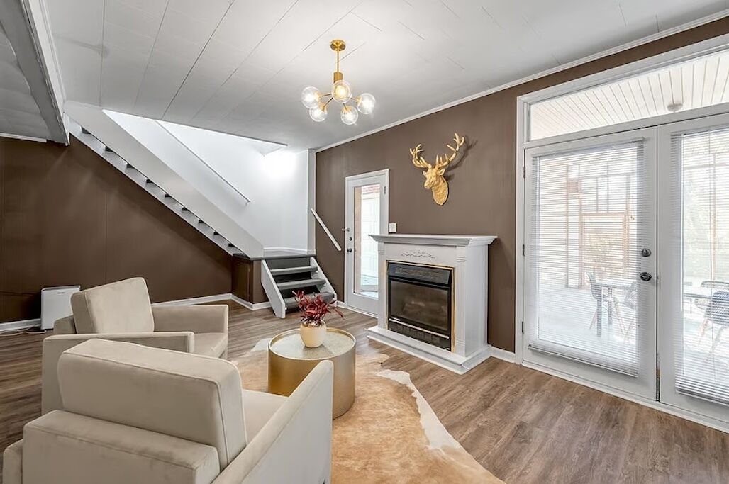 Ein modernes Wohnzimmer mit Kamin, Treppe und großem Fenster mit Jalousien.