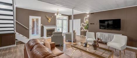 A modern living room with a brown leather sofa, a glass coffee table, and a flat-screen TV mounted on the wall.