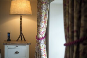 A bedside table with a lamp and a mobile phone, a floral curtain, and a partially visible door. - Boyne House Slane (Meath)
