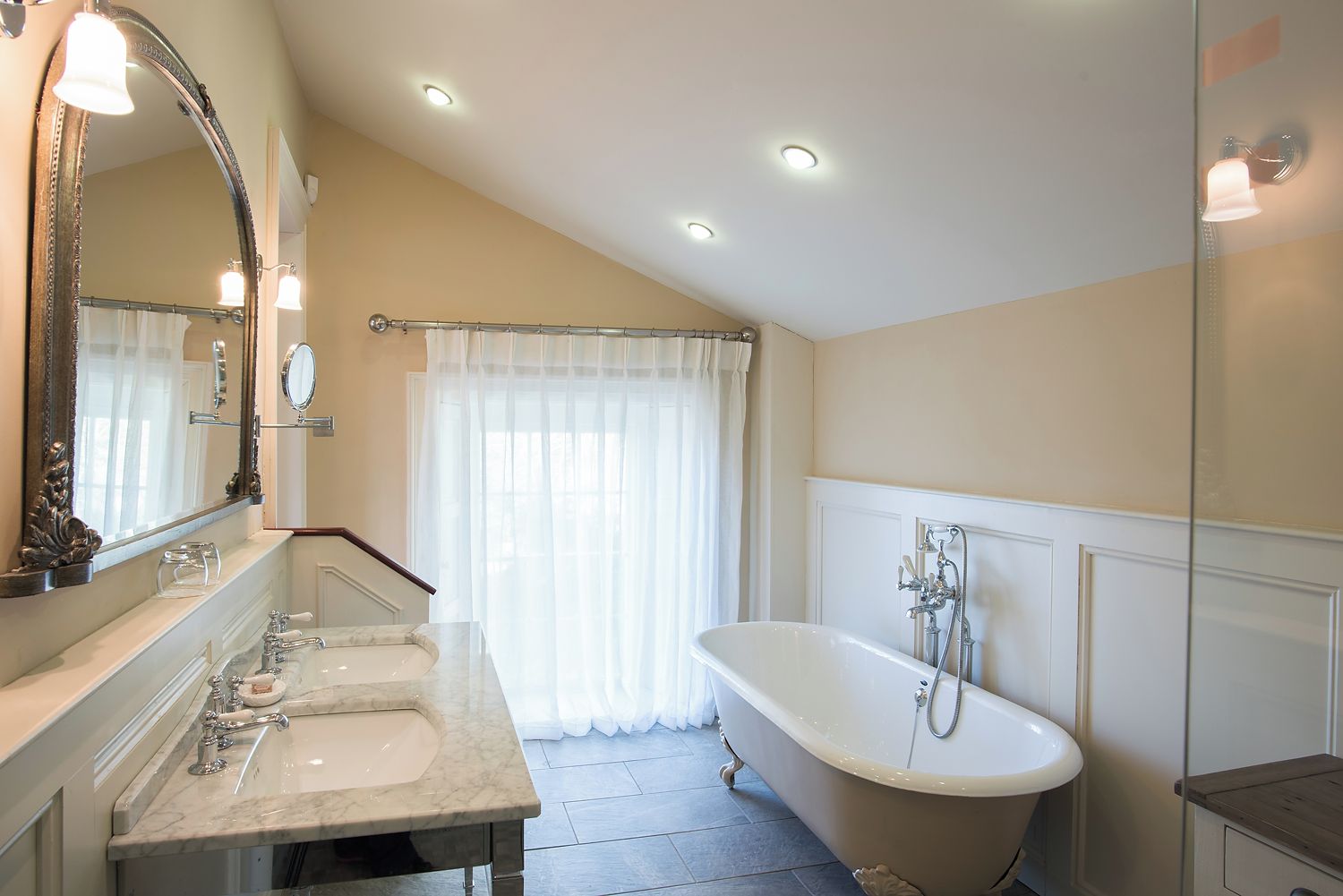 A bathroom with a freestanding bathtub, a large mirror, and a vanity with two sinks.