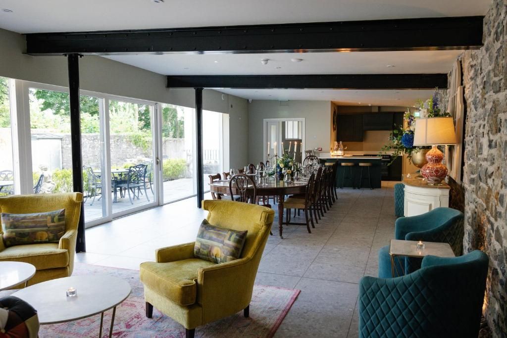 Un comedor amplio con una larga mesa y sillas, una cocina al fondo y vistas al exterior.