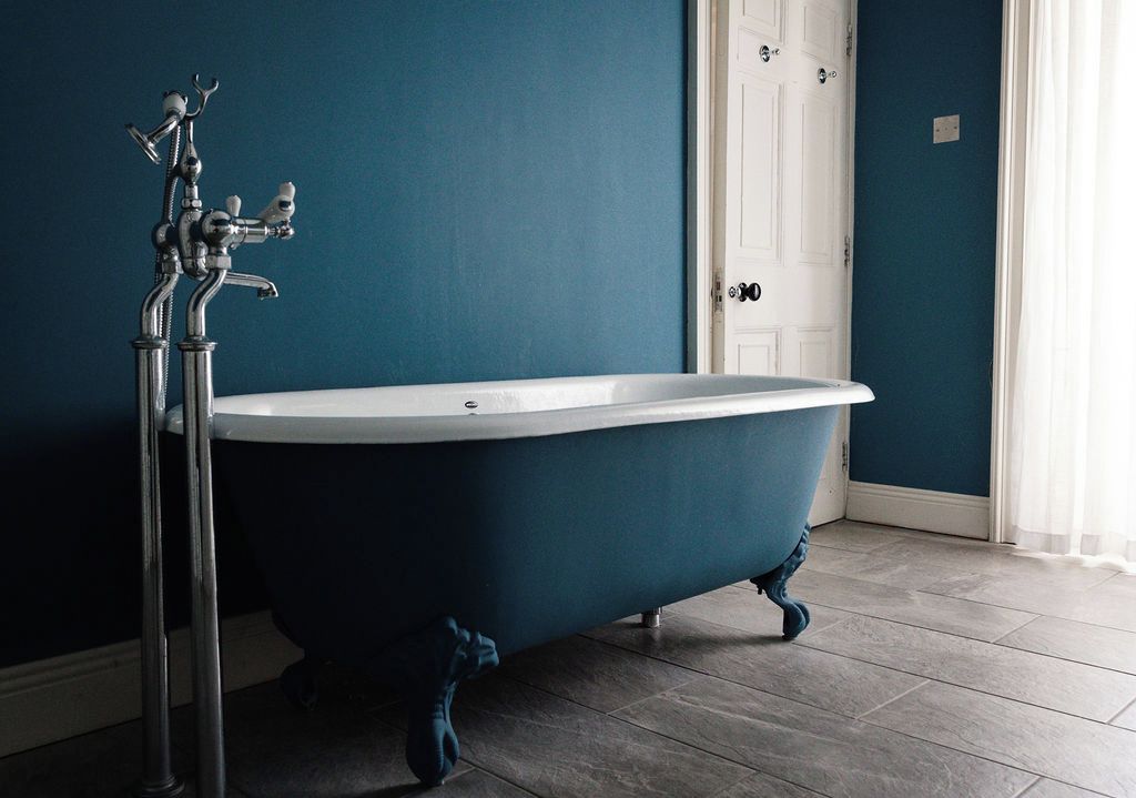 A clawfoot bathtub in a bathroom with a white door and a blue wall.