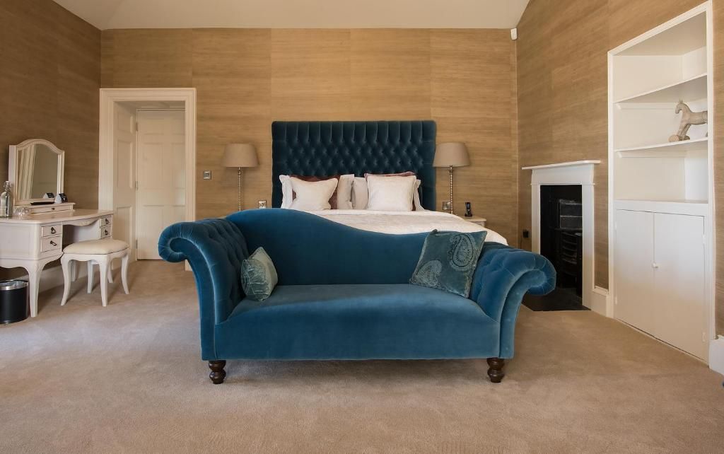 Quarto com uma cama grande, um sofá azul, cômoda, espelho e lareira.