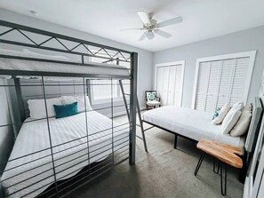 Ein Stockbett mit Schreibtisch und Stuhl, Deckenventilator und Fenster mit Rollläden.