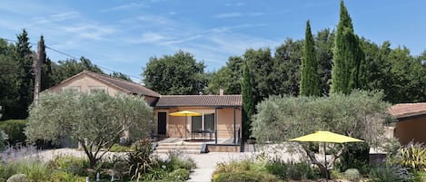 A house with a patio, a yellow umbrella, and a garden with various plants.