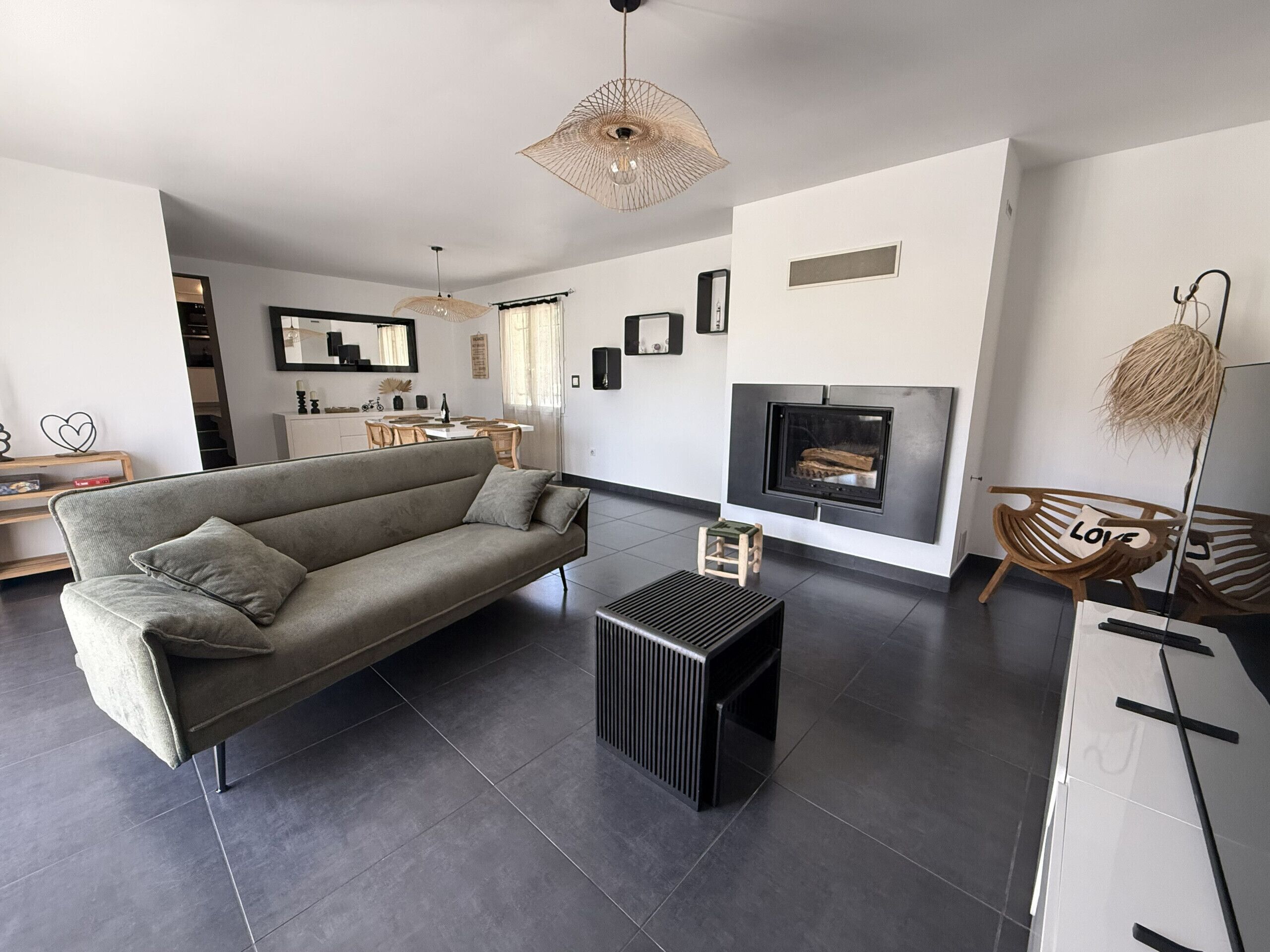 A modern living room with a sofa, a coffee table, a fireplace, and a dining area in the background.