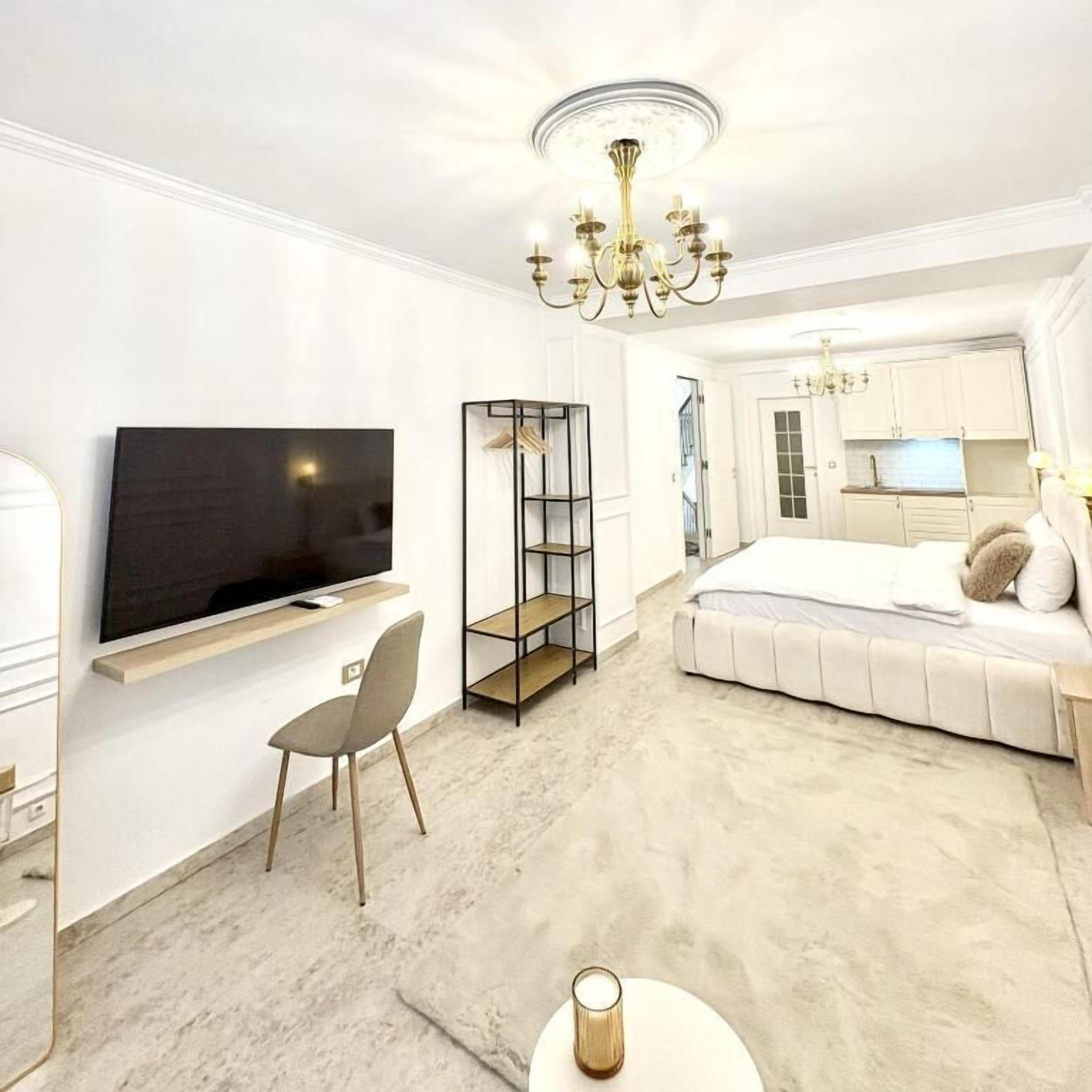 Una habitación de hotel moderna con televisor de pantalla plana, sofá cama, escritorio pequeño y candelabro.