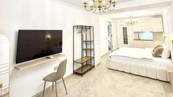 Una habitación de hotel moderna con televisor de pantalla plana, sofá cama, escritorio pequeño y candelabro.
