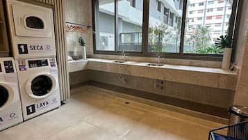 Un lavadero con dos lavadoras, un lavabo y una ventana con vistas a una zona residencial.